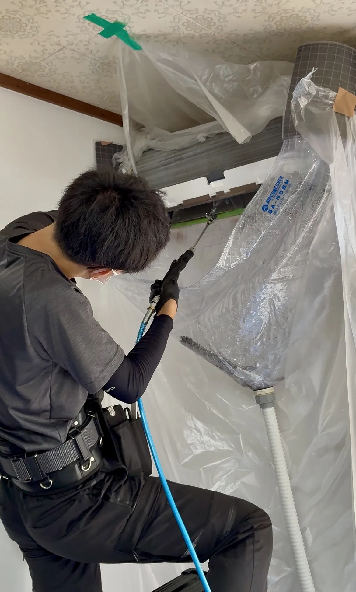 天井付近に設置されたエアコン室内機を養生シートで保護しながら作業するくらし屋山口のスタッフ