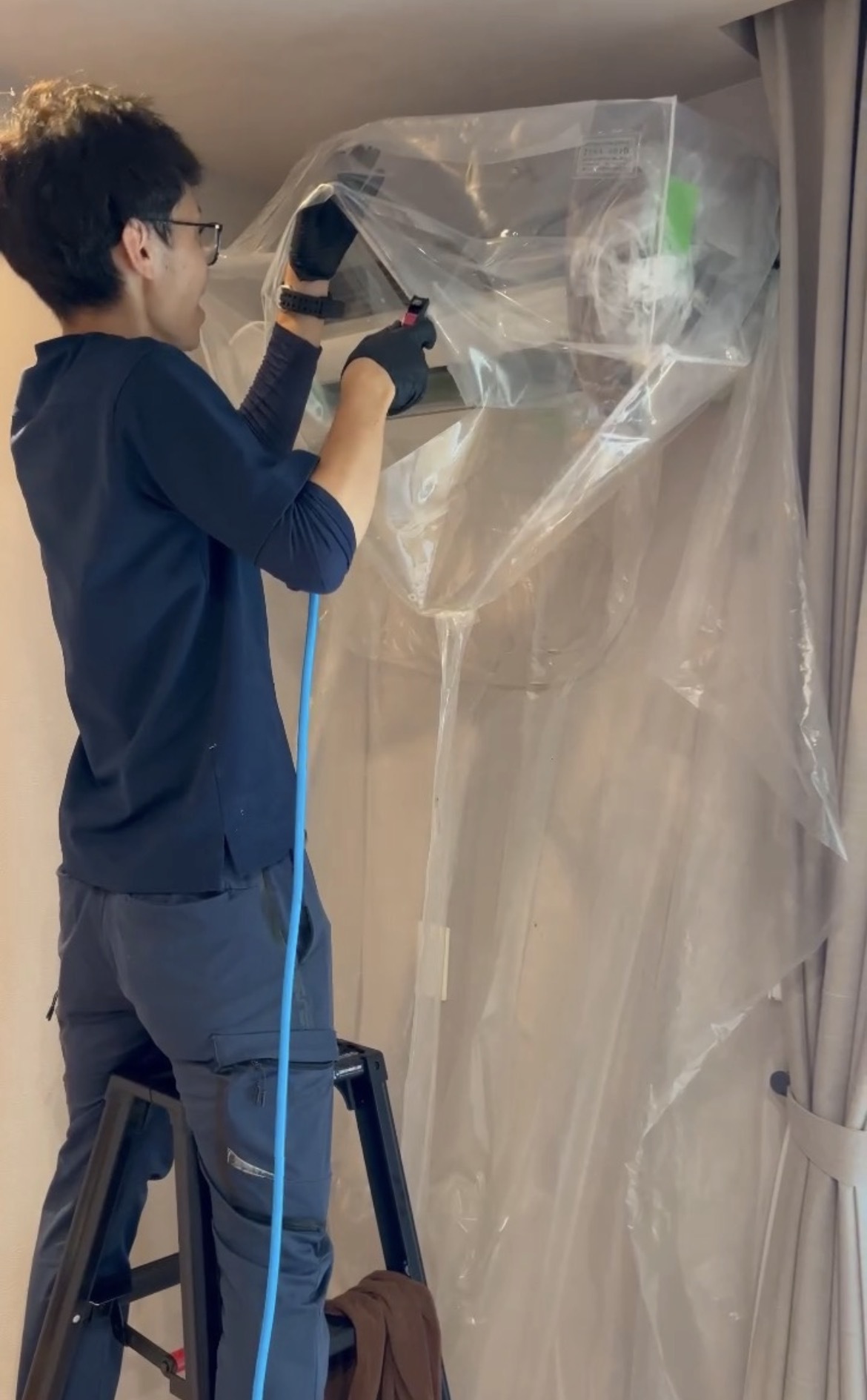 脚立に乗り、エアコン室内機をビニールシートで養生するスタッフ